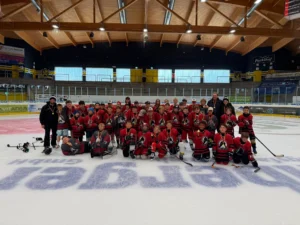 Gruppenfoto aller Teilnehmer in roten Camptrikots auf dem Eis beim Eishockeycamp Helmut de Raaf in Bad Tölz