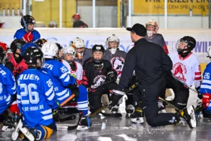 Trainer erklärt einer knienden Gruppe junger Eishockeyspieler die nächste Übung