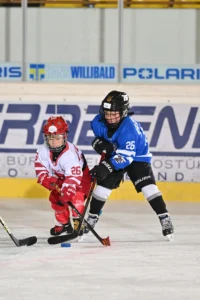 Junge Spieler in Rot-Weiß und Blau kämpfen vor der Bande um den Puck