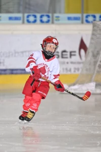 Kind im rot-weißen Trikot läuft konzentriert mit dem Puck übers Eis