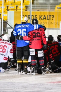 Teams in blauen und roten Trikots feiern gemeinsam auf dem Eis
