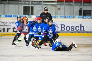 Spieler in Blau jubeln in einer Traube, einer liegt lachend auf dem Eis