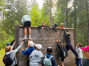 Kinder helfen sich gegenseitig beim Teamspiel über eine Holzwand im Wald